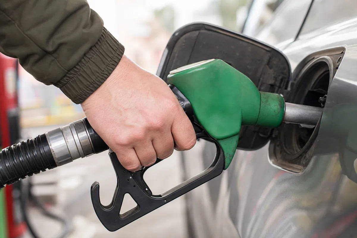 Main insérant un pistolet de carburant dans le réservoir d’une voiture à une station-service française en bord de route